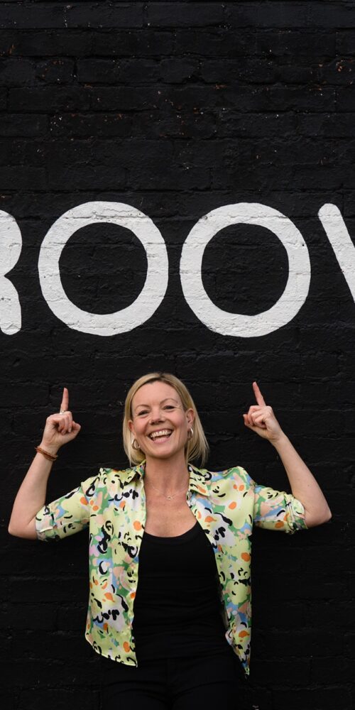 Emma from Drum and Bounce, Birmingham drum and bass workouts, wearing a floral shirt and pointing at a sign that says 'groove'