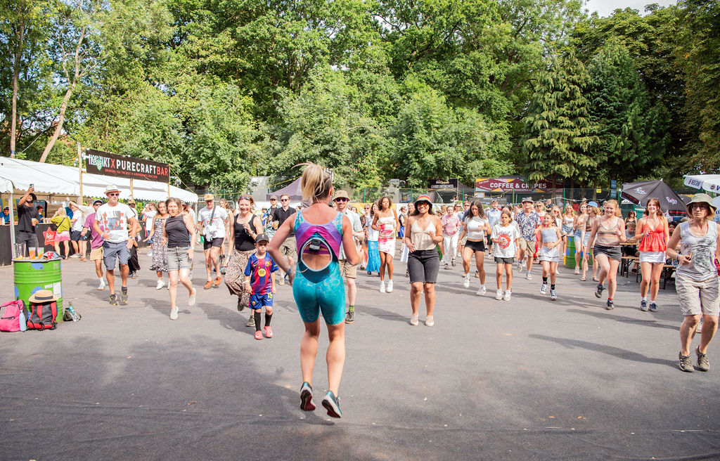Emma Smallman hosting a Drum n Bounce class in a festival environment with a diverse crowd enjoying the routine. 